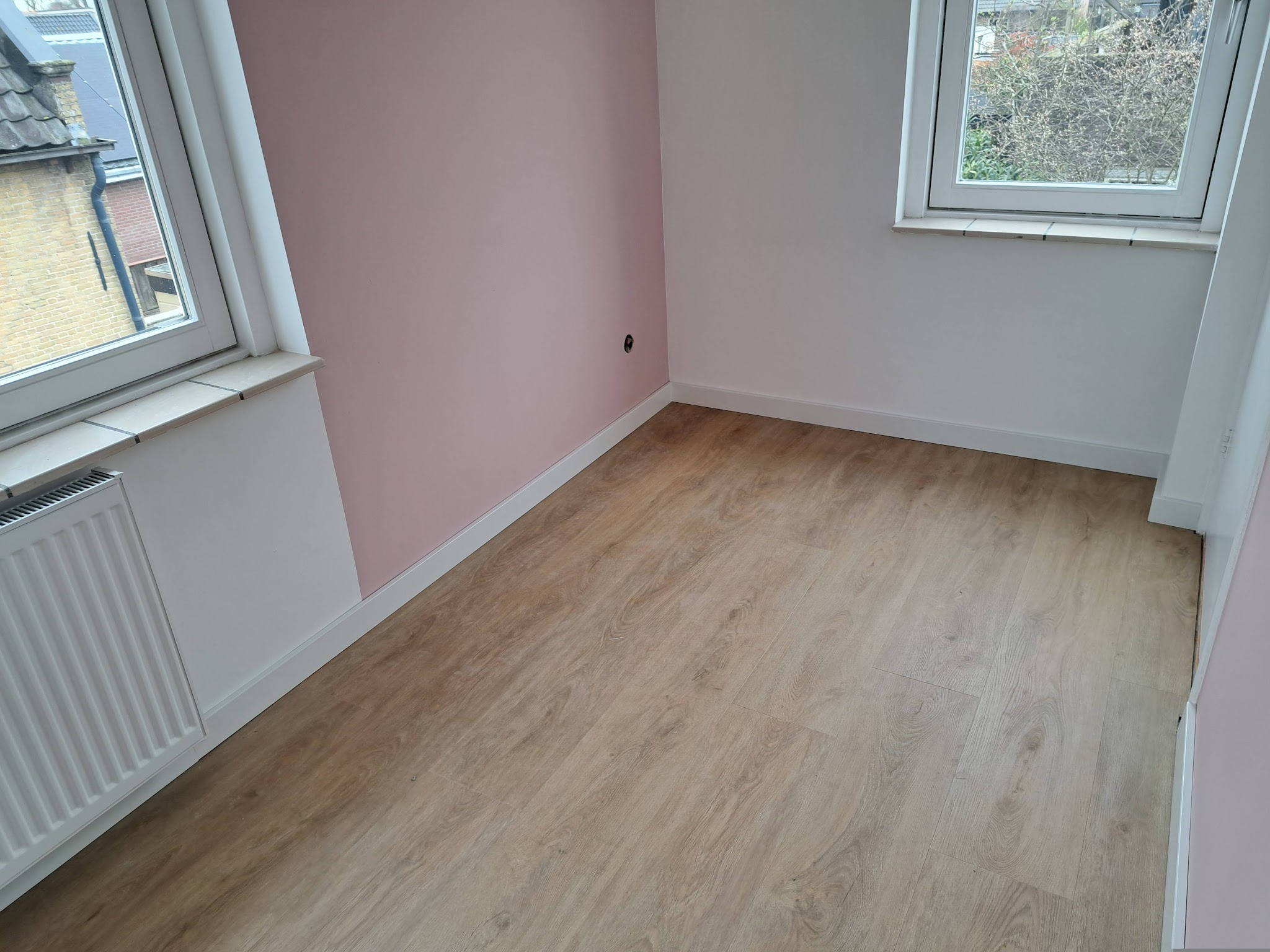 Gerenoveerde kamer met roze accentwand en laminaatvloer